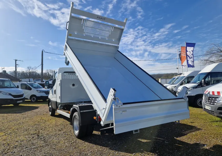 Vue arrière en léger contre-plongée d’un Iveco Daily blanc avec benne acier relevée et coffre latéral visible.