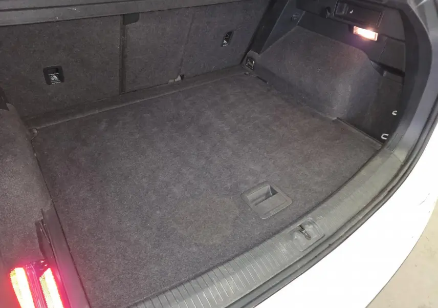 Coffre ouvert du Volkswagen Tiguan blanc, montrant le plancher modulable et l'éclairage intérieur à droite.