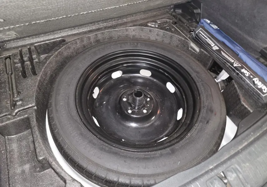 Gros plan sur la roue de secours noire dans le coffre modulable du Volkswagen Tiguan blanc.