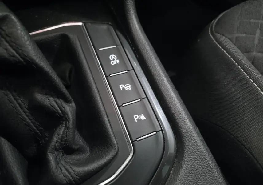 Gros plan sur la console centrale noire avec boutons de contrôle et partie de la sellerie tissu du Volkswagen Tiguan blanc.