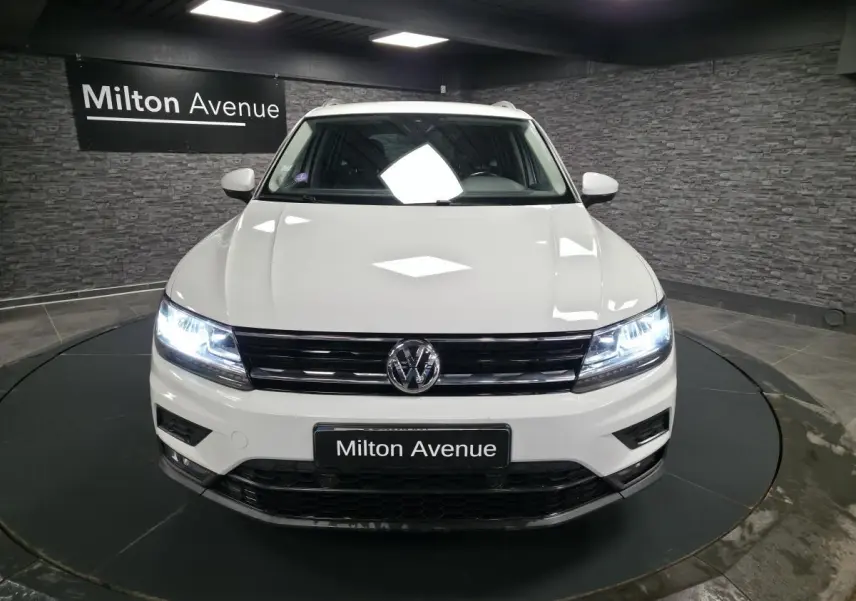Vue de face du Volkswagen Tiguan blanc avec phares LED allumés dans un showroom au mur en pierre grise.