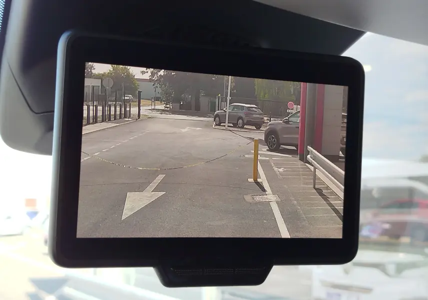 Vue de la caméra de recul du Renault Kangoo blanc, affichant une zone de stationnement avec flèche au sol et barrières.