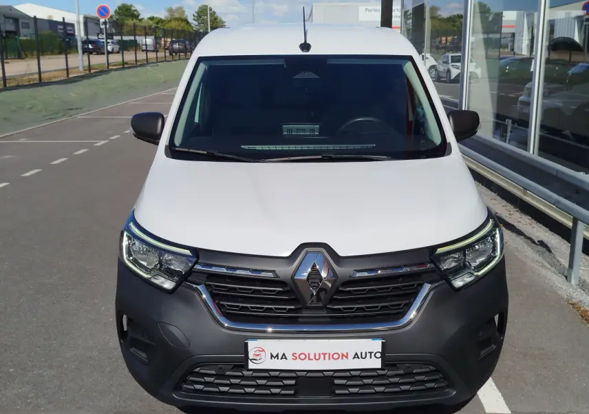 Vue avant d'un Renault Kangoo blanc minéral 2023 avec calandre noire et phares LED allumés, stationné en extérieur.
