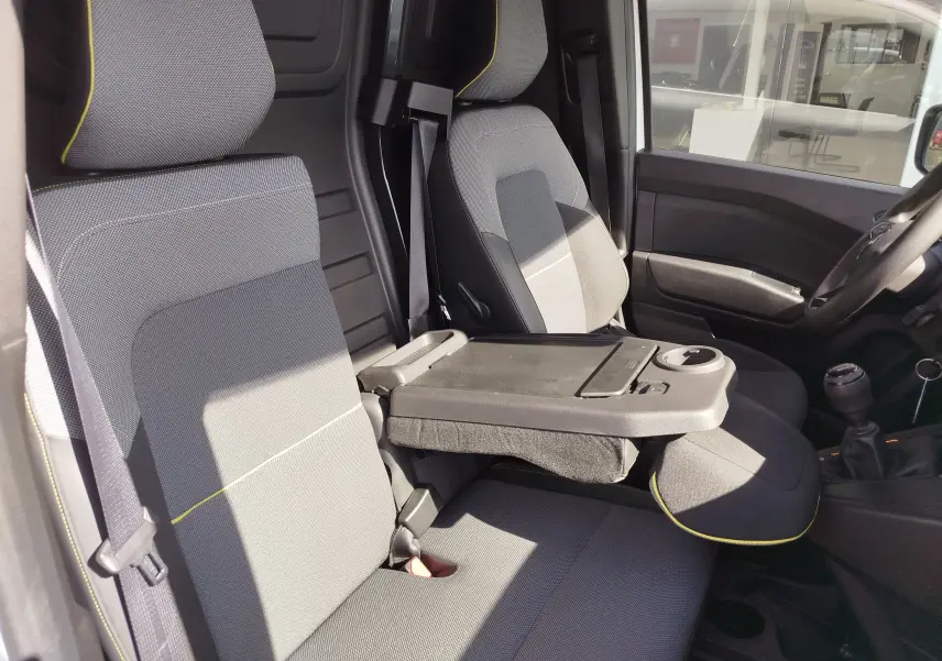 Intérieur avant droit du Renault Kangoo 2023 blanc, sièges gris avec surpiqûres jaunes et tablette rabattable centrale.