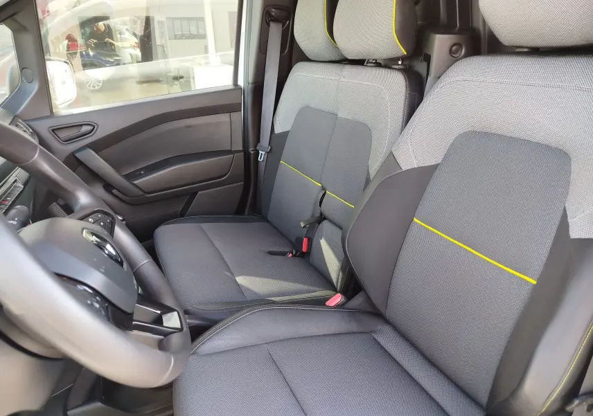 Vue intérieure côté conducteur du Renault Kangoo 2023, sièges gris avec surpiqûres jaunes et volant multifonction.