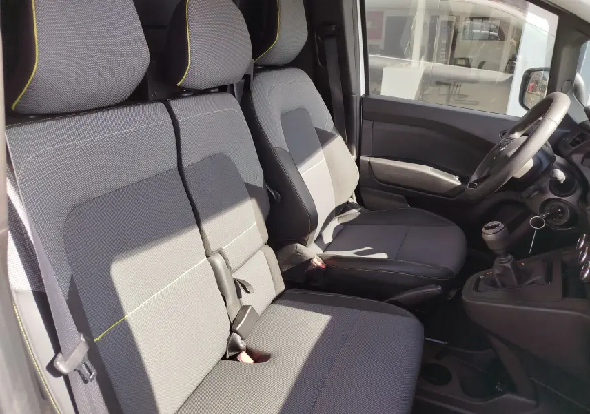 Vue intérieure côté conducteur du Renault Kangoo 2023, sièges gris avec surpiqûres jaunes et volant multifonction.