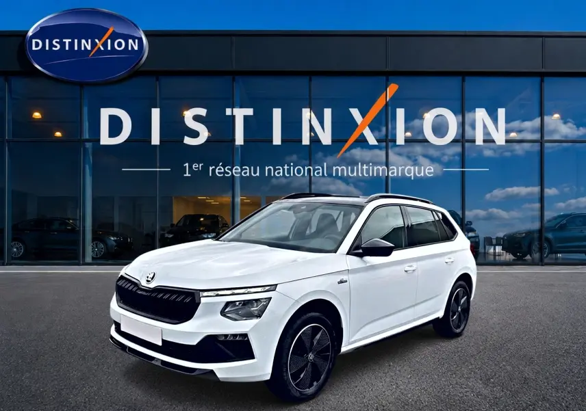 Skoda Kamiq blanc nacré en 3/4 avant droit, avec jantes noires et toit panoramique visible.