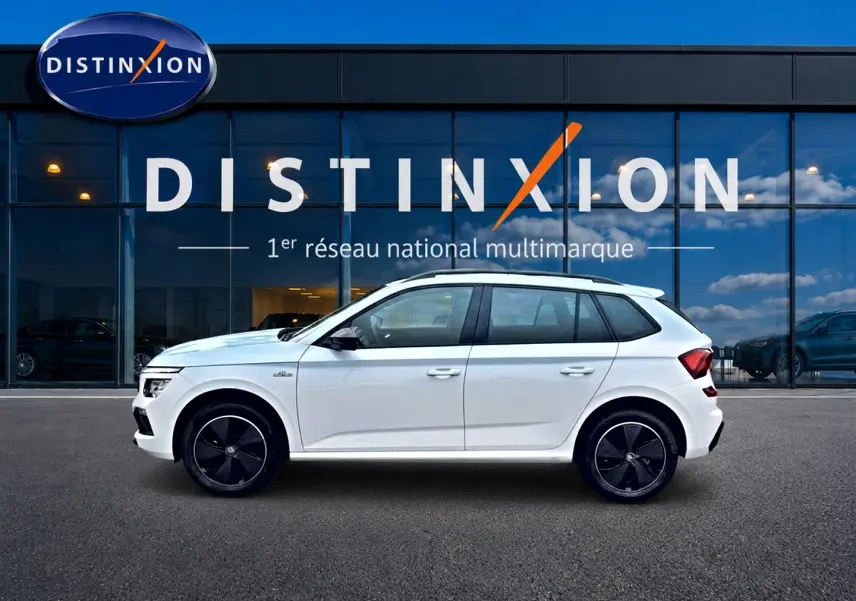 Profil droit d’un Skoda Kamiq blanc nacré 2026 avec jantes noires et toit blanc devant un showroom Distinxion.