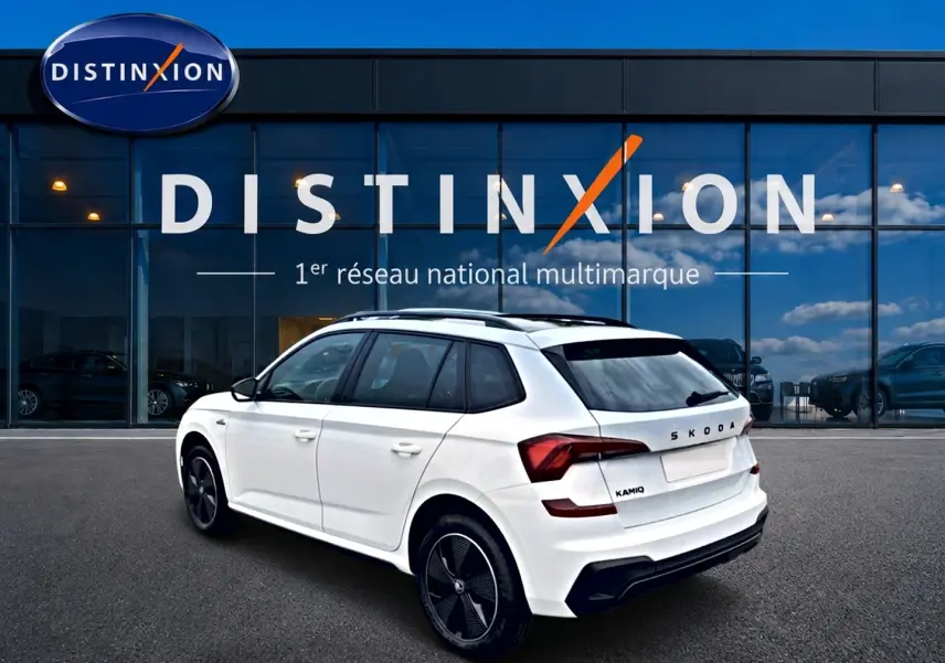 Vue 3/4 arrière droite d'un Skoda Kamiq blanc nacré avec jantes noires et toit panoramique, devant une vitrine Distinxion.