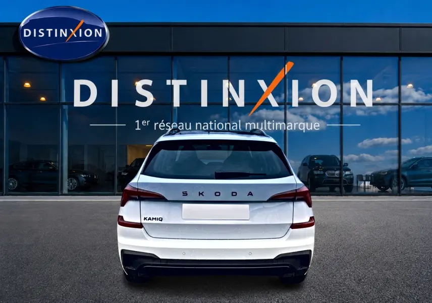 Vue arrière d'un Skoda Kamiq blanc nacré avec logo distinctif et diffuseur noir, devant une vitrine Distinxion.