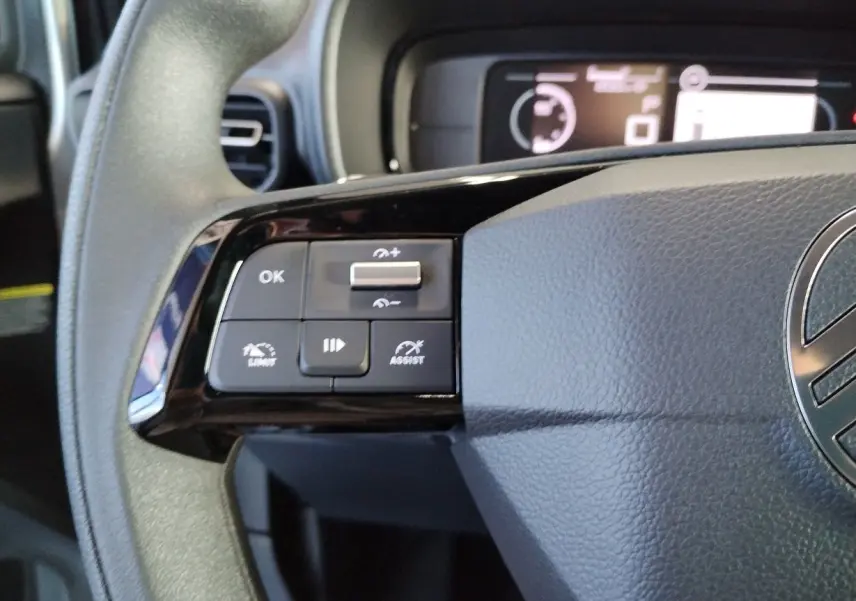 Gros plan sur les commandes à gauche du volant gris du Citroën Berlingo 2025 avec affichage numérique en arrière-plan.