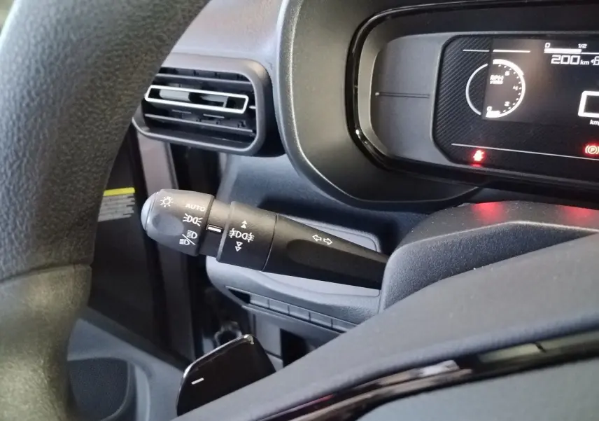 Gros plan sur la commande des feux et clignotants à gauche du volant dans le tableau de bord du Citroën Berlingo gris acier 2025.