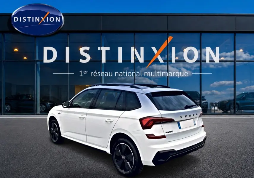Vue 3/4 arrière droite d'un Skoda Kamiq blanc nacré avec jantes noires et toit panoramique, devant une vitrine Distinxion.