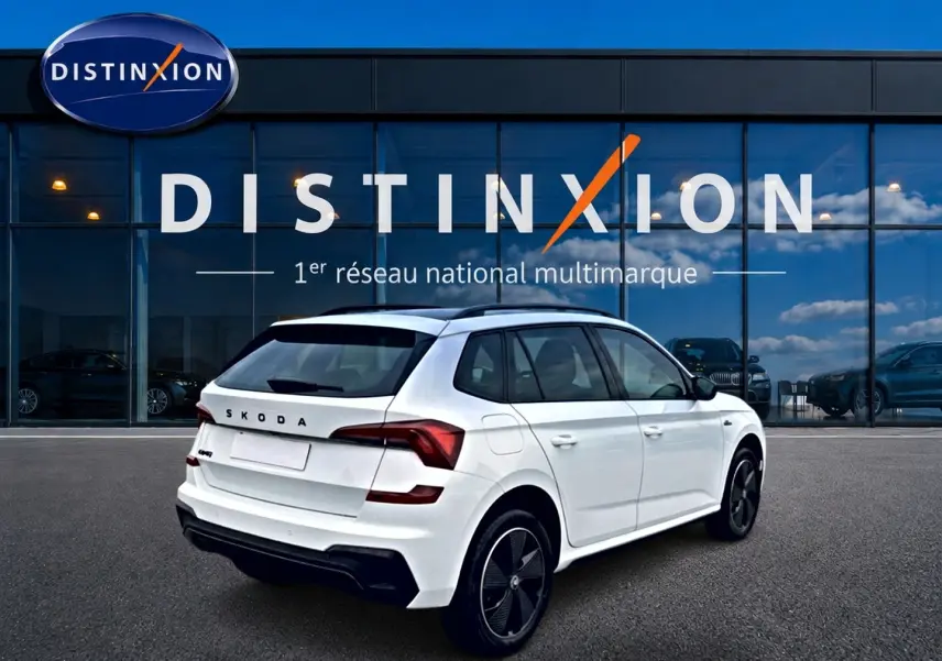 Vue 3/4 arrière droite d’un Skoda Kamiq blanc nacré avec jantes noires et toit panoramique, devant une vitrine Distinxion.