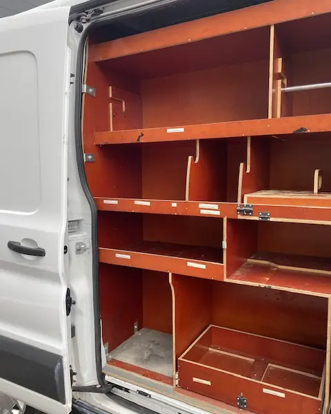 Vue partielle du fourgon Ford Transit blanc 2019, montrant l'intérieur aménagé avec étagères en bois côté droit ouvert.