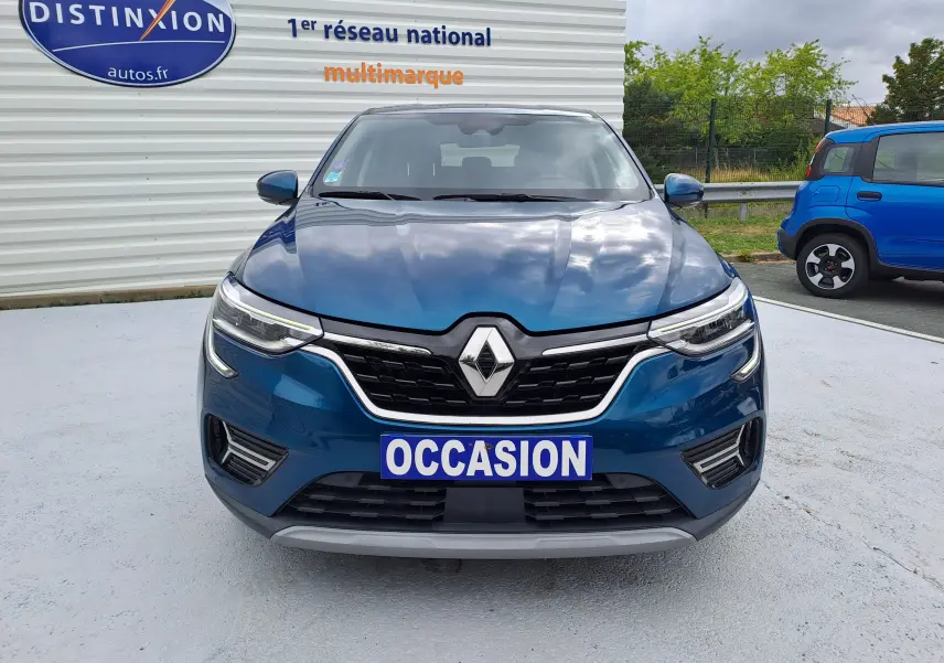 Vue frontale d'une Renault Arkana bleu Zanzibar métal avec calandre noire et logo Renault central, plaque "OCCASION" visible.
