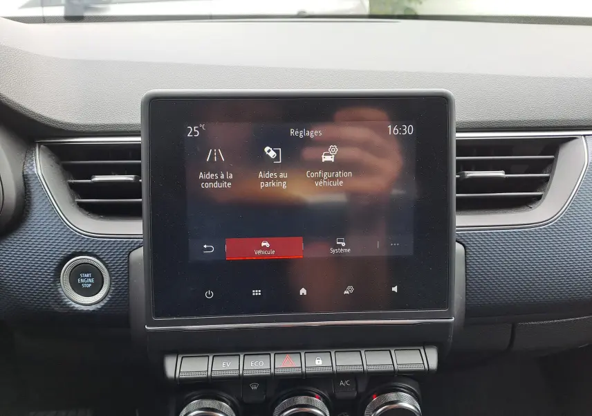 Écran tactile central du tableau de bord du Renault Arkana bleu Zanzibar, avec commandes climatisation et démarrage moteur visible.