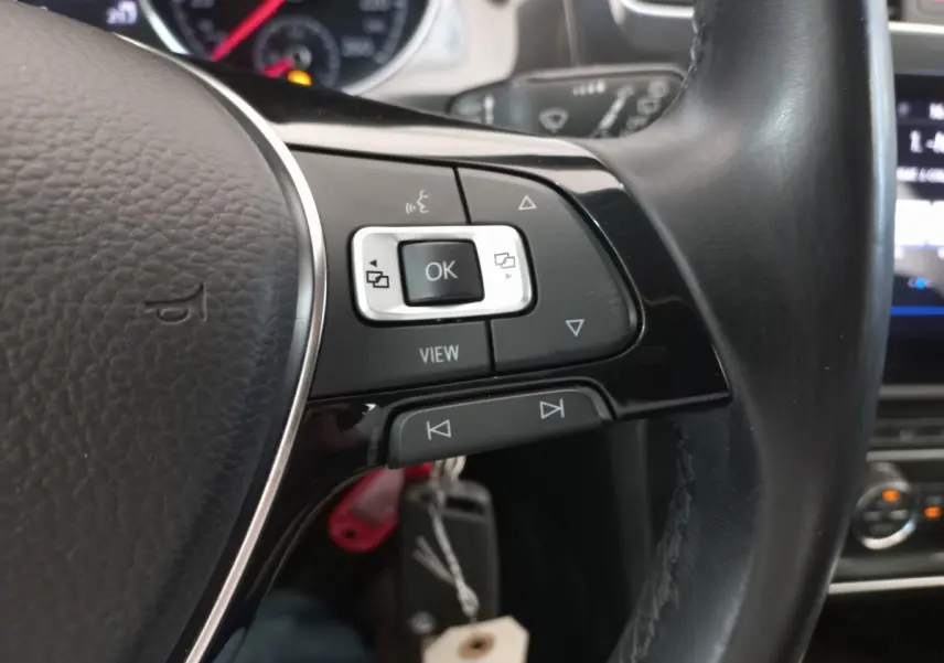 Gros plan sur les commandes gauche du volant cuir noir d'une Volkswagen Golf gris foncé, avec tableau de bord en arrière-plan.