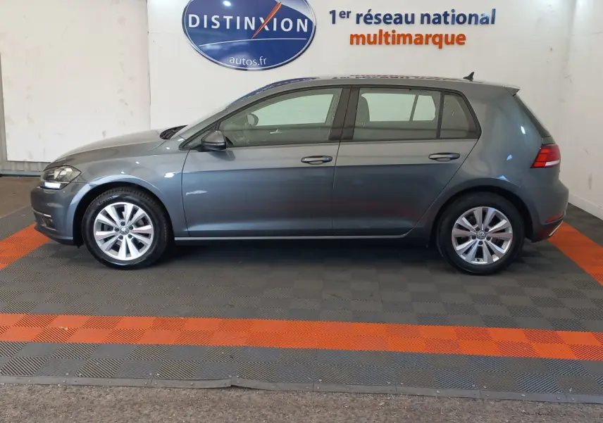 Profil droit d'une Volkswagen Golf gris foncé 2019 garée en intérieur sur sol à damier gris et orange.