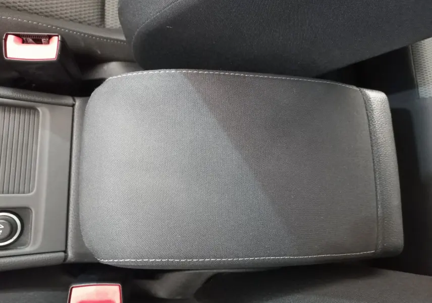 Accoudoir central en tissu gris foncé dans l'habitacle d'une Volkswagen Golf 2019, avec ceintures de sécurité rouges visibles.