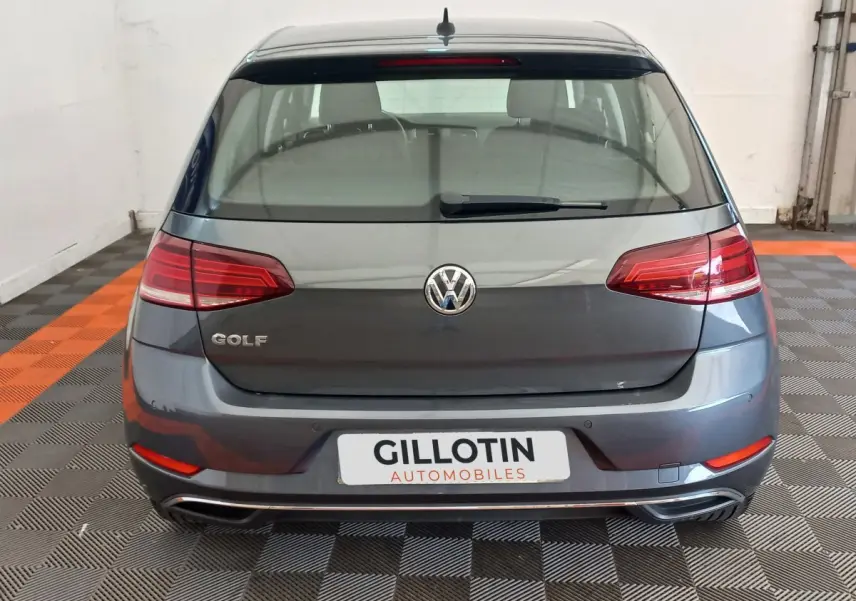 Vue arrière d'une Volkswagen Golf gris foncé stationnée sur un sol à damiers noir et orange, avec feux arrière LED.