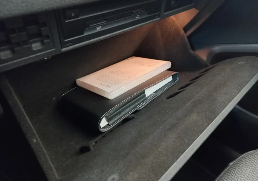 Vue rapprochée de la boîte à gants ouverte d'une Volkswagen Golf gris foncé, avec un manuel et une pochette noire à l'intérieur.