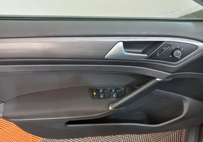 Vue rapprochée de la porte côté gauche de la Volkswagen Golf gris foncé avec commandes électriques et poignée argentée.