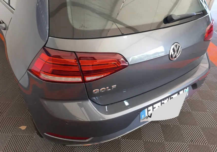 Vue arrière en 3/4 gauche d'une Volkswagen Golf gris foncé avec feux arrière LED et logo distinctif sur le coffre.