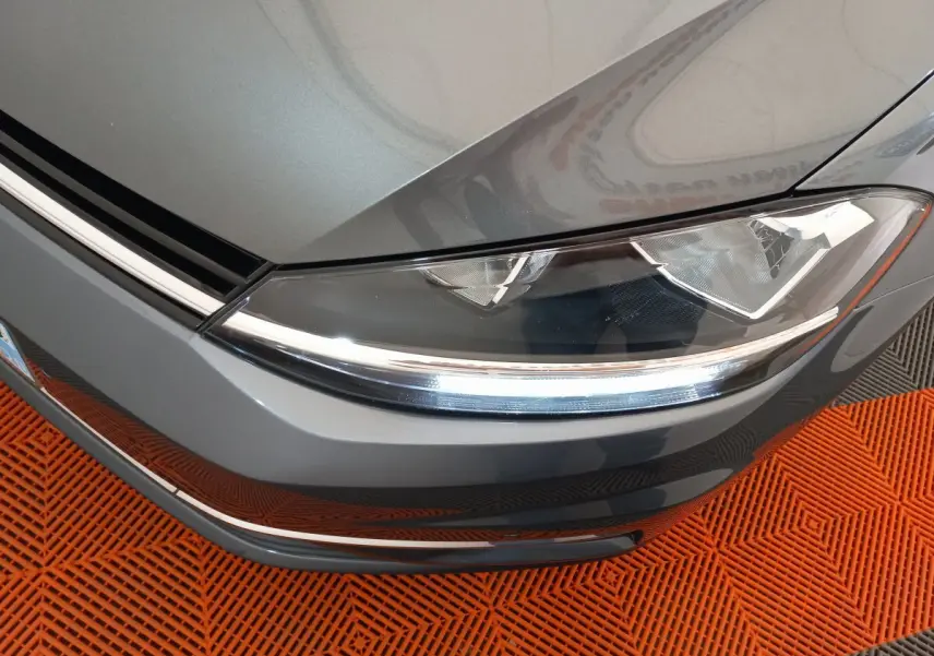 Gros plan sur le phare avant droit d'une Volkswagen Golf gris foncé 2019, avec détails LED et calandre visible.