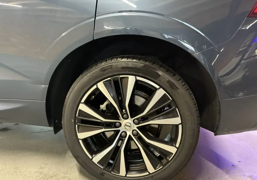 Gros plan sur la roue arrière droite d’un Volvo XC60 bleu 2023 avec jante alliage 20'' noir et diamant.