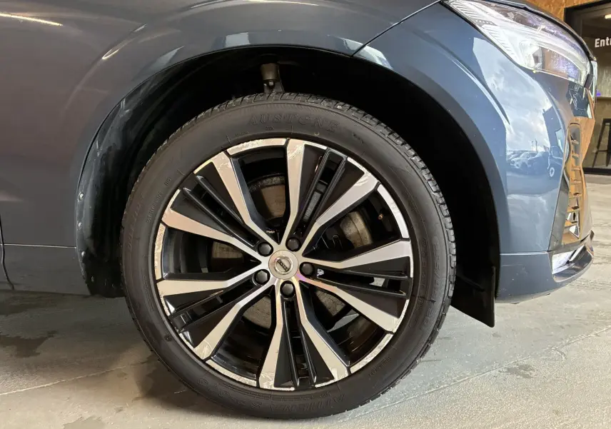 Gros plan sur la roue avant gauche du Volvo XC60 bleu 2023 avec jante alliage 20'' noir et diamant.