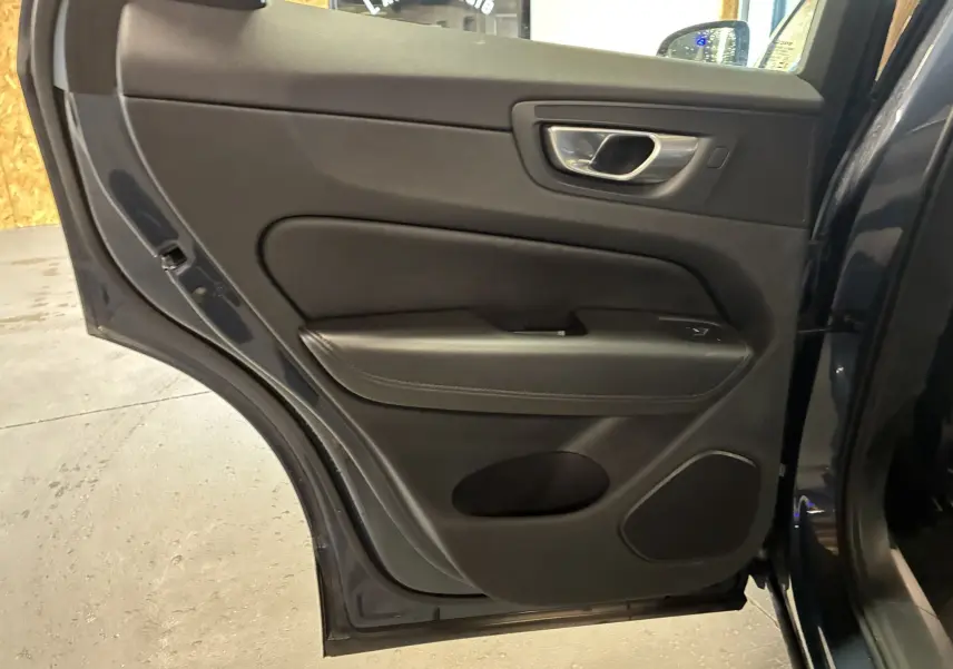 Vue intérieure de la porte arrière droite du Volvo XC60 bleu 2023 avec garniture noire et poignée chromée.