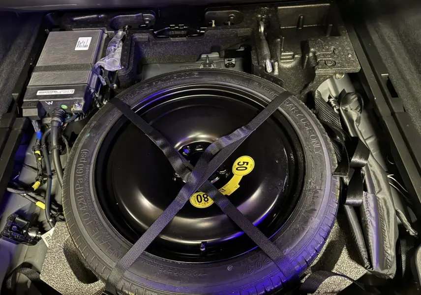 Vue rapprochée de la roue de secours galette noire dans le coffre du Volvo XC60 2023, entourée d’équipements et câblages.