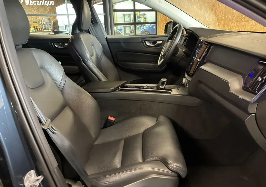 Vue intérieure côté gauche du Volvo XC60 2023 bleu, sièges cuir noirs et planche de bord simili-cuir avec console centrale moderne.