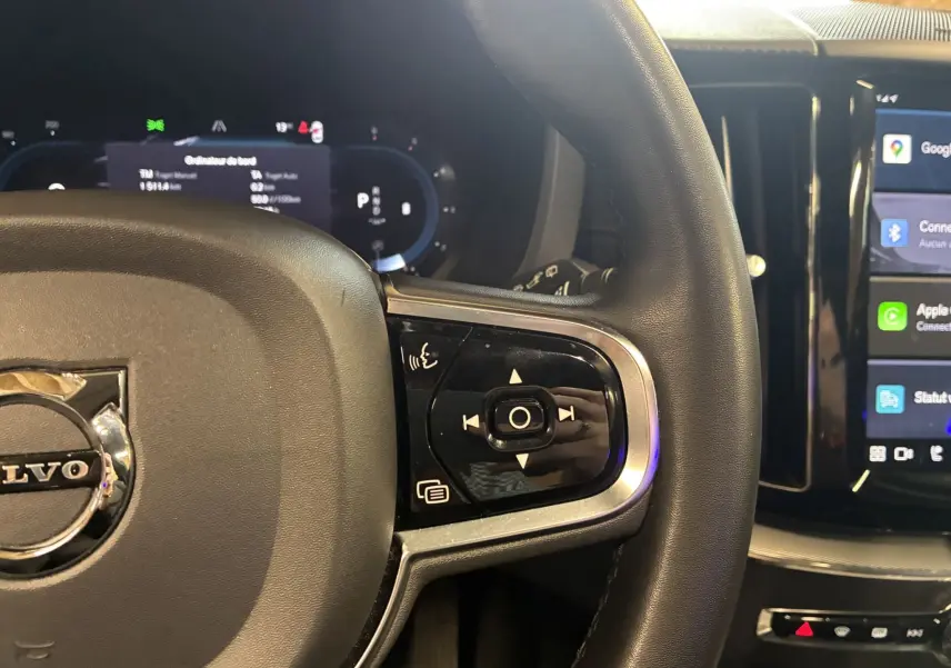 Gros plan sur le volant noir du Volvo XC60 2023 avec commandes multifonctions et écran tactile de la console centrale.