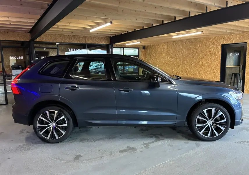 Vue latérale droite d'un Volvo XC60 bleu 2023 avec jantes alliage 20'' bicolores et rétroviseurs noirs laqués.
