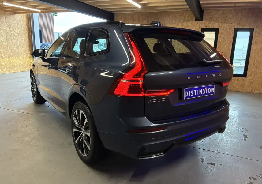 Vue 3/4 arrière droite du Volvo XC60 bleu 2023 avec feux arrière en L et jantes alliage 20 pouces bicolores.