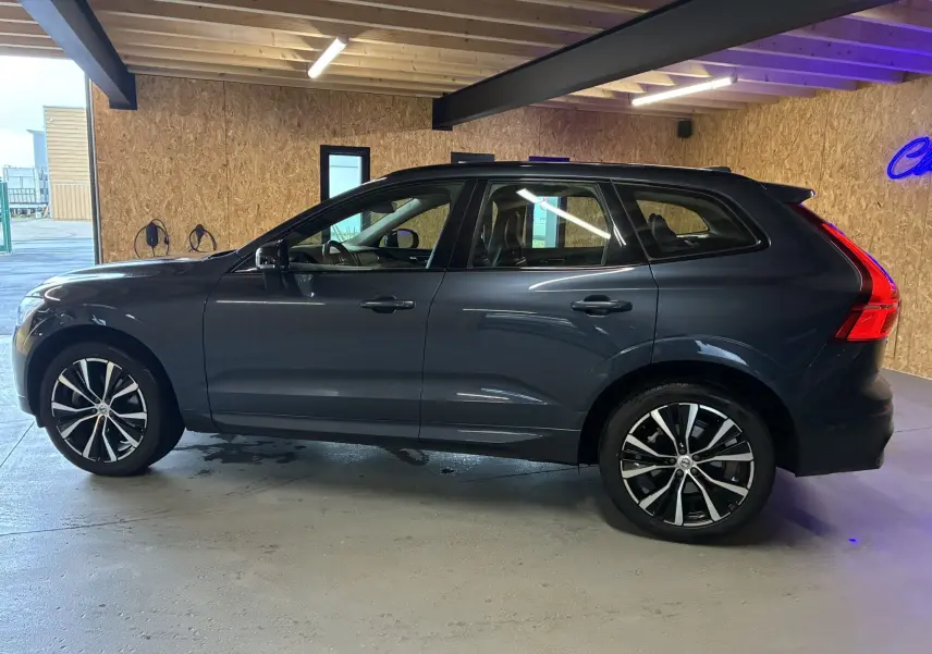 Vue latérale droite d'un Volvo XC60 bleu 2023 avec jantes alliage 20'' noir et diamant dans un garage.
