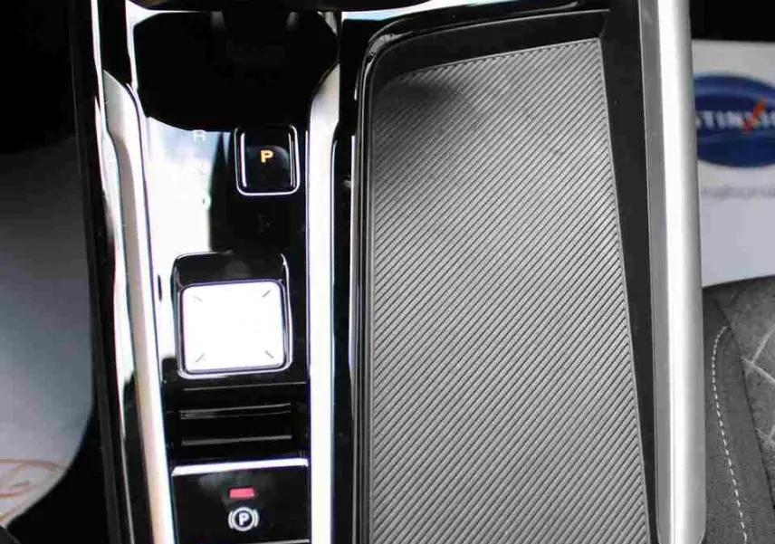 Vue en plongée sur la console centrale noire brillante du MG ZS 1.5L Hybrid+ avec levier de vitesses électronique et surface texturée.