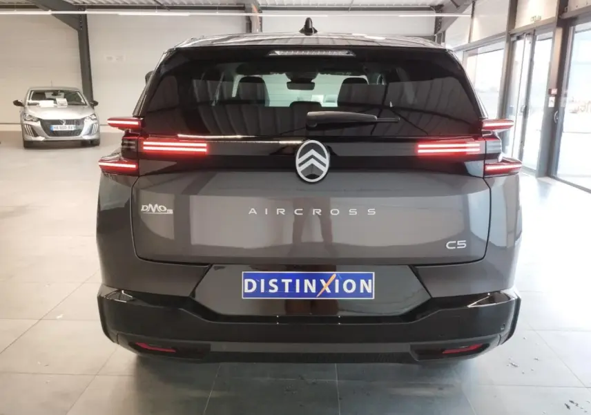 Vue arrière d'un Citroën C5 Aircross gris platine avec feux arrière LED distinctifs allumés en intérieur showroom.
