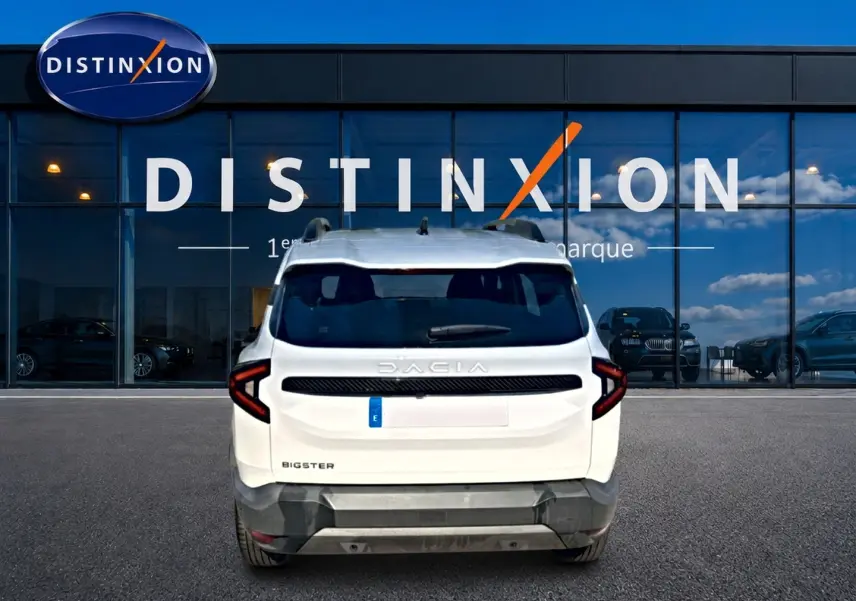 Vue arrière d'un Dacia Bigster blanc 2026 avec feux LED en forme de C et barres de toit visibles, devant une vitrine Distinxion.