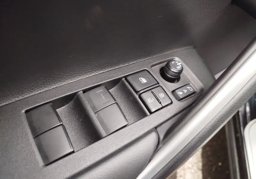 Gros plan sur les commandes des vitres et rétroviseurs côté conducteur d'une Toyota Corolla Cross Hybrid 140 Luxury Limited noire.