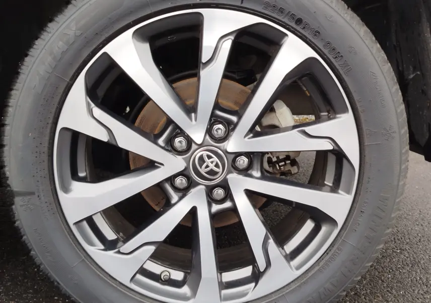 Gros plan sur la jante alliage bi-ton argent et noir avec logo Toyota, montée sur un pneu 225/50 R18 du Corolla Cross noir.