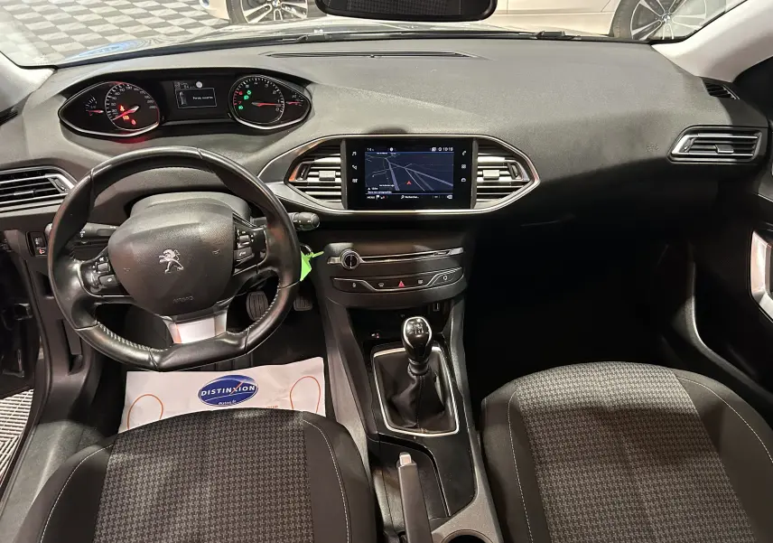 Vue intérieure avant de la Peugeot 308 Active Pack 2021, avec tableau de bord noir, volant multifonction et écran tactile central.