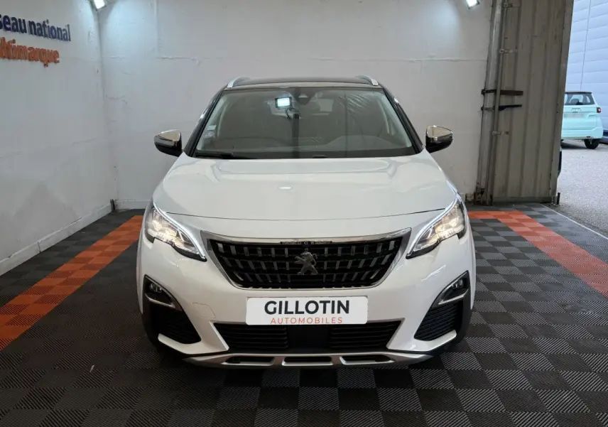Peugeot 3008 blanc vue de face dans un garage avec calandre noire et phares allumés.