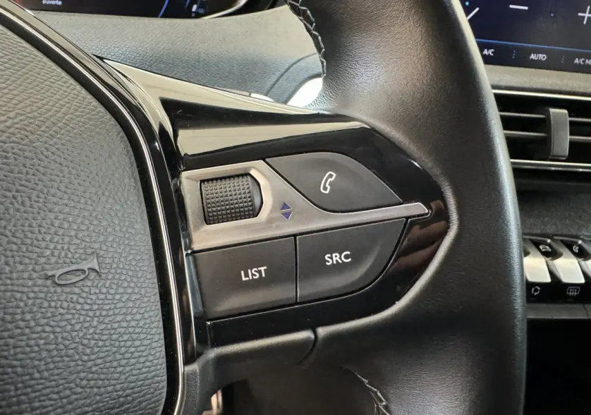 Gros plan sur les commandes gauche du volant cuir noir du Peugeot 3008 blanc, avec tableau de bord et écran tactile en arrière-plan.