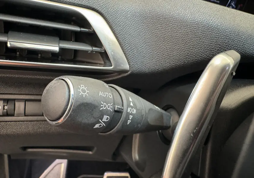 Gros plan sur la commande d'éclairage noire à gauche du volant dans l'habitacle d'un Peugeot 3008 blanc.