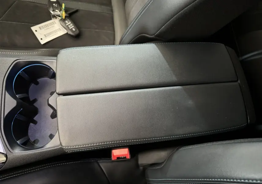 Gros plan sur l'accoudoir central noir avec surpiqûres bleues et porte-gobelets du Peugeot 3008 blanc 2019.