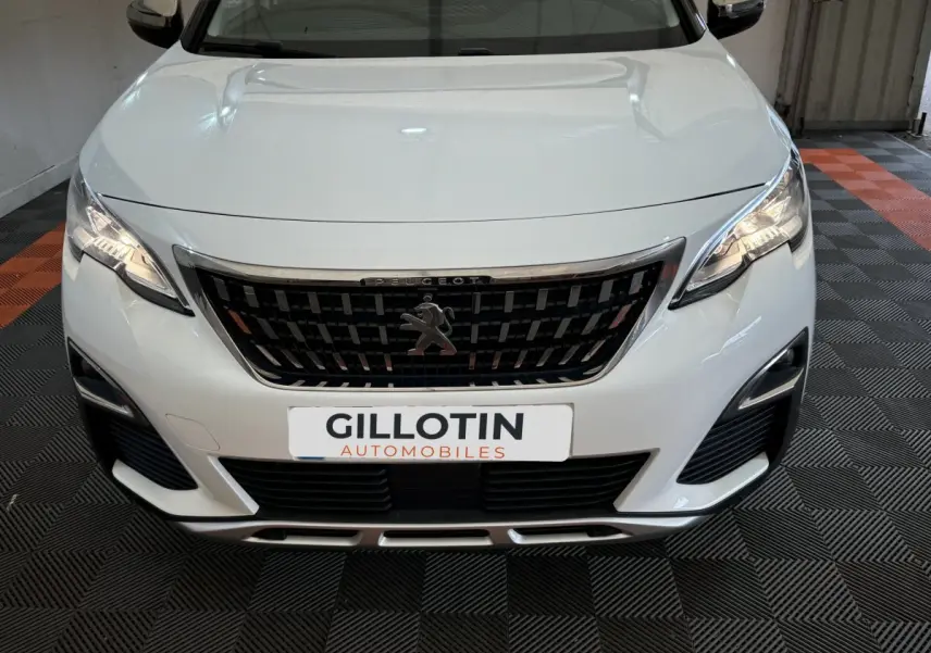 Vue avant rapprochée d’un Peugeot 3008 blanc avec calandre noire et phares LED allumés en intérieur.