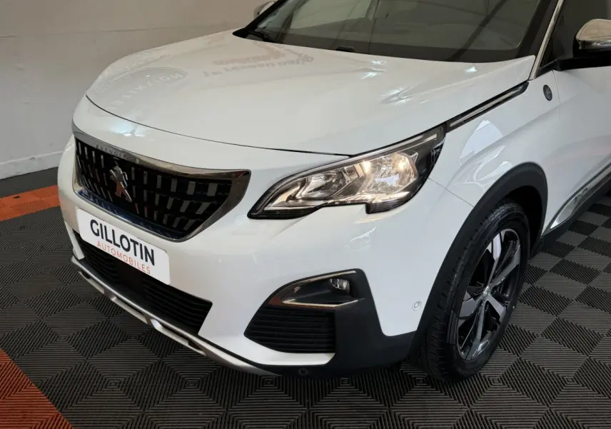 Vue 3/4 avant droit d'un Peugeot 3008 blanc avec calandre noire et phares allumés sur sol carrelé noir et orange.